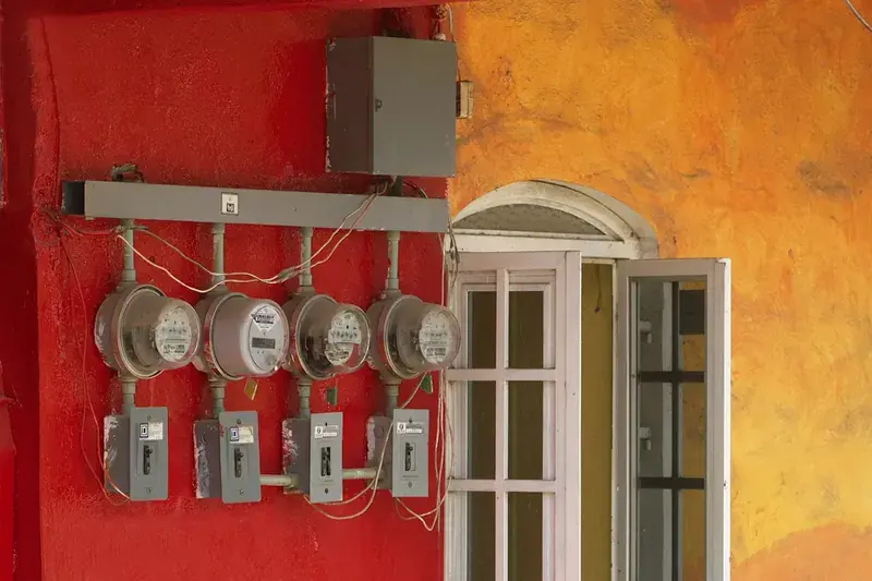 Four electricity meters mounted on a red wall beside a window