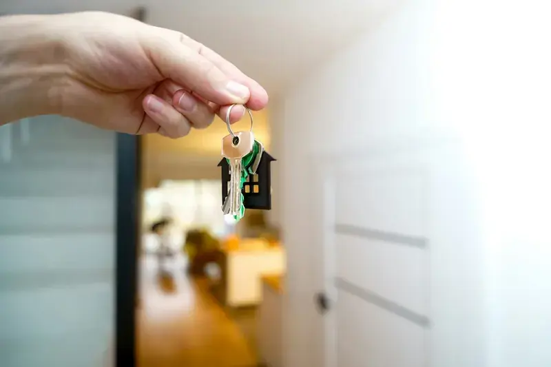 Hand holding house keys with a small house-shaped keyring inside a home entrance