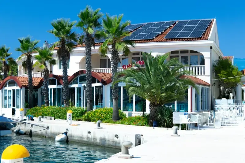 White house with rooftop solar panels, palm trees and a marina in front